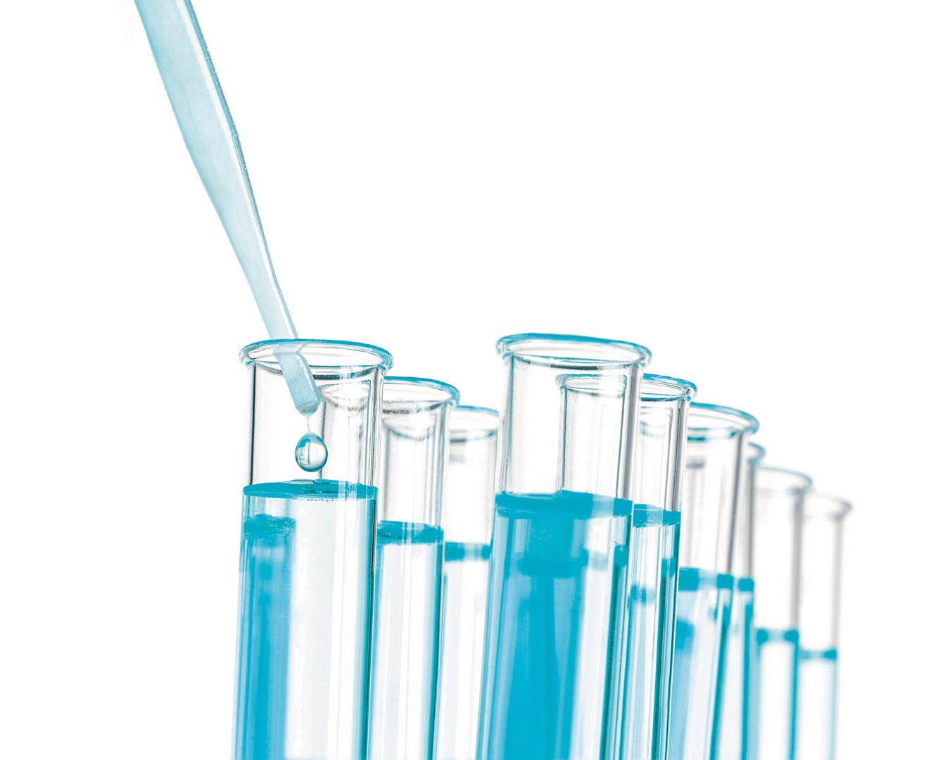 A glass dropper depositing a drop of liquid in one of several clear glass tubes full of a light blue liquid