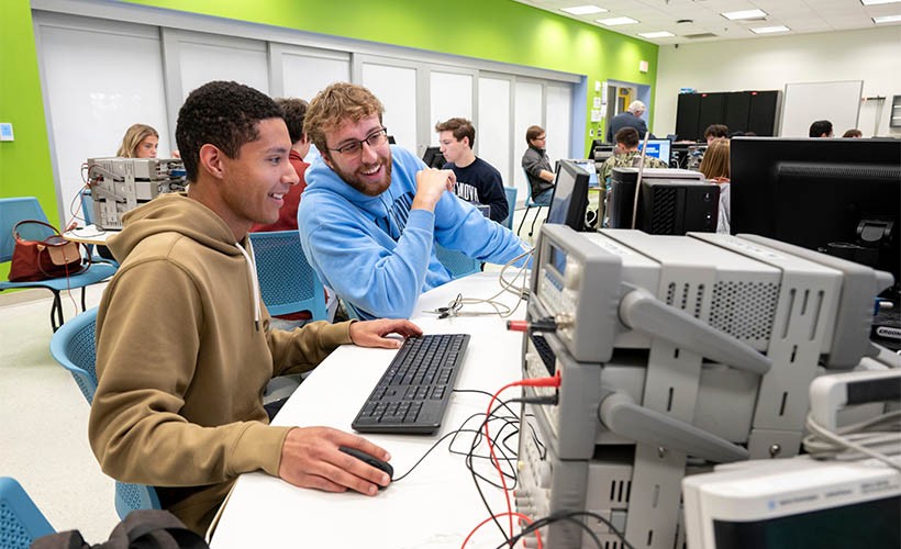 Two students sit at a desk with a computer