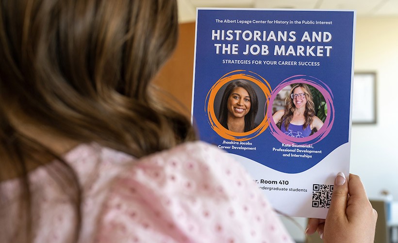 A student reads a poster about a History career event. A student reads a poster about a History career event.