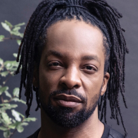 Image of Jericho Brown looking directly into the camera in front of a dark gray background. 
