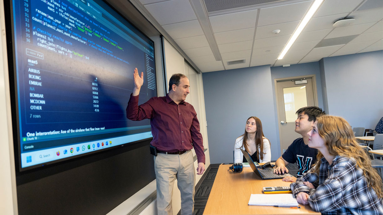 Professor pointing at screen while speaking to students