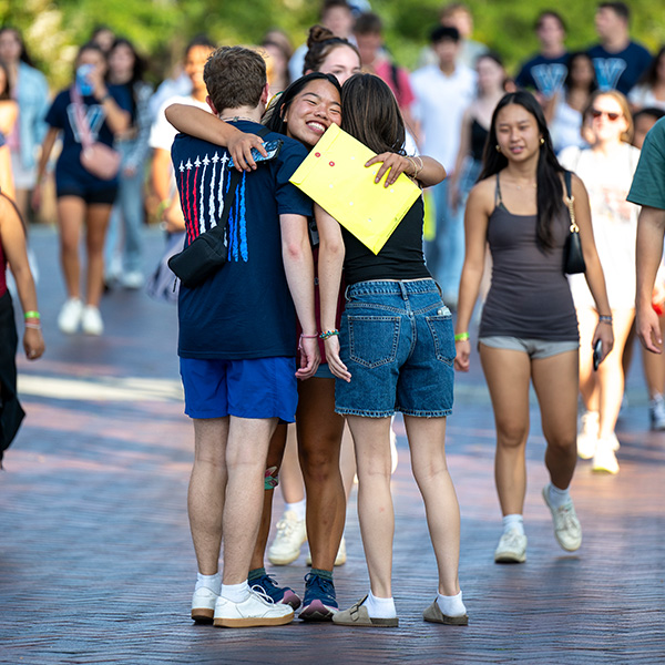 A young woman smiles while hugging her two friends outside. 